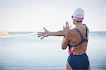 Female open water swimmer stretching arm and shoulder at ocean