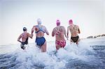 Female open water swimmers running and splashing in ocean surf