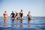 Female open water swimmers walking, wading in sunny ocean