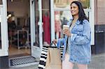 Smiling woman walking along storefront with coffee and shopping bags