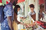 Worker helping couple shopping for fruit at storefront sidewalk