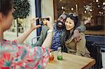 Woman photographing affectionate couple friends with camera phone at sidewalk cafe