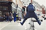 Playful young businessman commuting, riding bicycle on sunny urban street