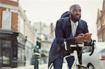 Pensive young businessman texting with cell phone, commuting with bicycle on urban street