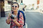 Portrait laughing, enthusiastic young female tourist in sunglasses photographing with camera on urban street