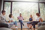 Male therapist with clipboard leading group therapy session