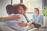 Smiling female therapist watching couple hugging in couples therapy session