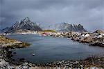 Fishing village at waterfront below snowy, rugged mountains, Reine, Lofoten, Norway