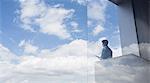 Pensive businessman standing on modern balcony looking at blue sky and clouds