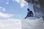 Businessman on modern balcony looking out window at blue sky and clouds