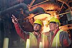 Steelworkers talking, pointing and looking away in steel mill