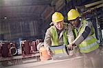 Steelworkers using laptop in steel mill