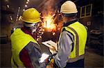 Steelworkers with digital tablet and clipboard talking in steel mill