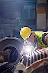 Focused steelworker with flashlight examining steel part in steel mill