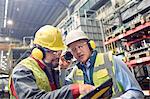 Steelworkers wearing ear protectors using digital tablet in steel mill