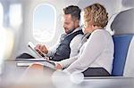 Businessman and businesswoman using digital tablet on airplane