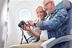 Mature couple looking at photos on digital camera on airplane