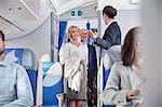 Flight attendant greeting passengers boarding airplane