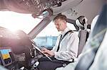 Male pilot with clipboard preparing in airplane cockpit