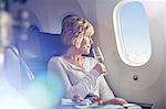 Mature woman drinking champagne, looking out window in first class on airplane