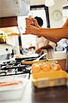 Woman cracking fresh pepper on eggs cooking on stove in kitchen