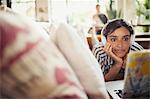 Young woman with headphones using laptop on living room sofa