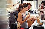 Smiling couple texting with smart phone, eating toast in kitchen