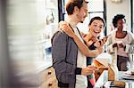 Affectionate couple hugging, texting with smart phone in kitchen