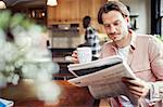 Man drinking coffee and reading newspaper in kitchen