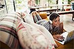 Smiling woman with headphones using laptop on sofa