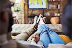 Affectionate couple holding hands, watching TV in living room