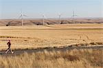 Man jogging on rural road, farmland and wind turbines in distance, Washington