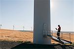 A wind farm technician standing and using a laptop at the base of a turbine on a wind farm in open countryside at Palouse.