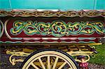 The painted decorated side panel of a bow top gypsy caravan and large wooden wheel.