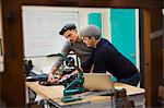 Two men, tailors leaning over a workbench discussing a project, planning their work.