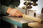 A craftsman using a machine drill on a piece of smooth planed shaped wood.