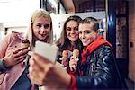 Three young women with ice cream cones taking smartphone selfie on city street