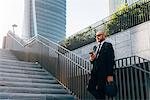 Mature businessman standing on steps, using smartphone, low angle view