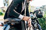 Mature businessman outdoors, leaning over motorcycle, doing up bag, mid section