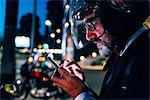 Mature businessman outdoors at night, wearing motorcycle helmet, using smartphone, profile
