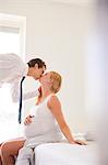 Pregnant woman kissing businessman husband in bedroom