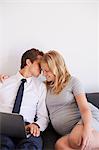 Romantic man whispering to pregnant girlfriend on sofa