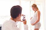 Over shoulder view of man photographing pregnant girlfriend on smartphone