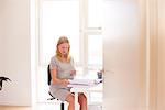 Pregnant young woman at desk looking at smartphone and paperwork