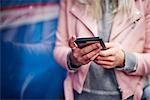 Mid section of young woman holding smartphone at city tram station