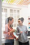 Two businesswomen laughing while taking a coffee break in office kitchen