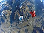 Aerial view of two wingsuit flyers, one on his back facing one in red suit flying above landscape