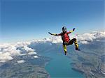 Female skydiver sitting up in free fall above clouds and lake