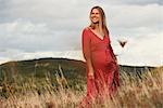 Portrait of happy pregnant woman in red dress on hillside