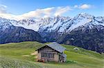 Meadows and wooden huts framed by snowy peaks at dawn, Tombal, Soglio, Bregaglia Valley, canton of Graubunden, Switzerland, Europe